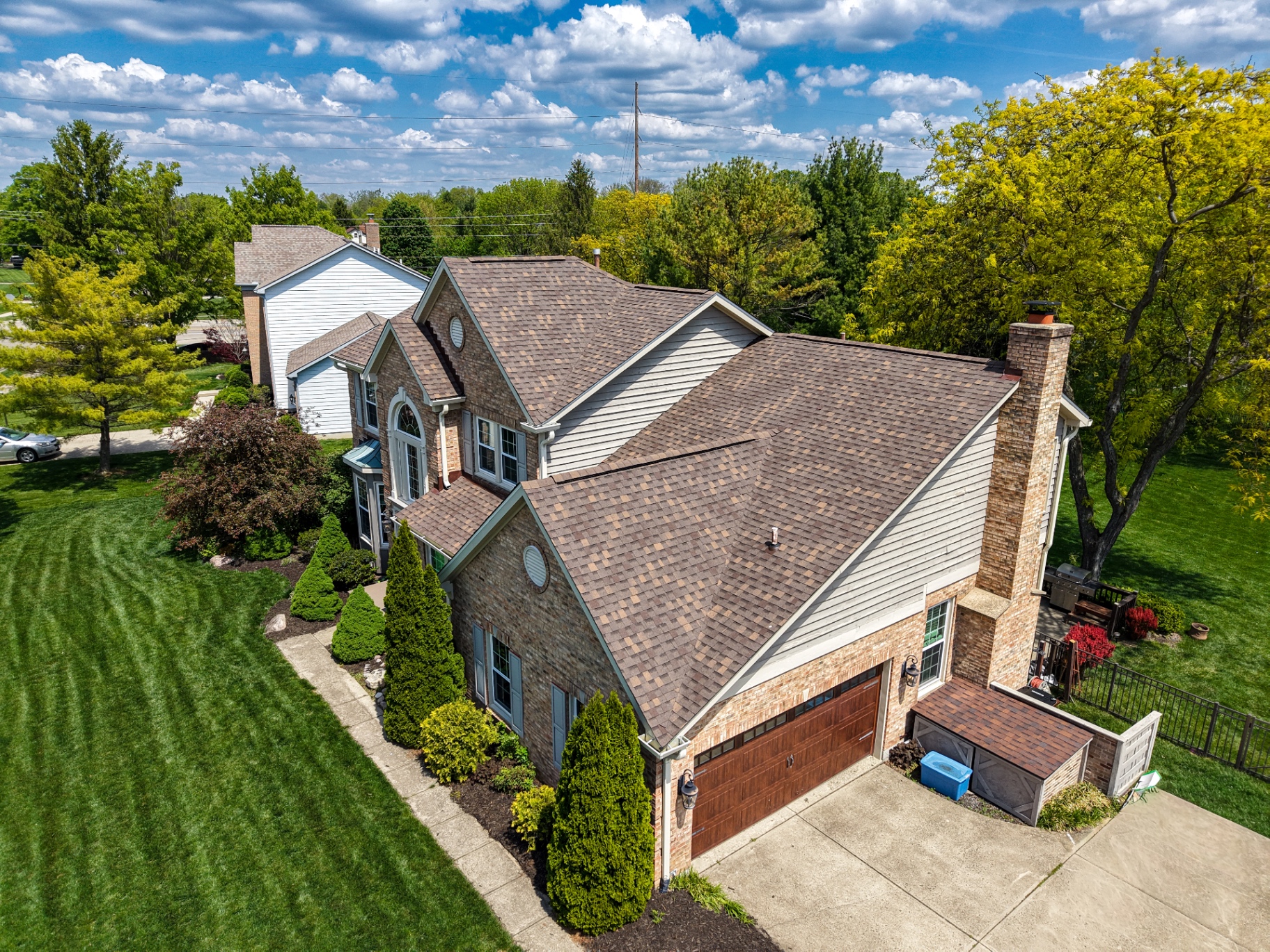 Aerial view of two-story brick home with manicured lawn and mature trees
