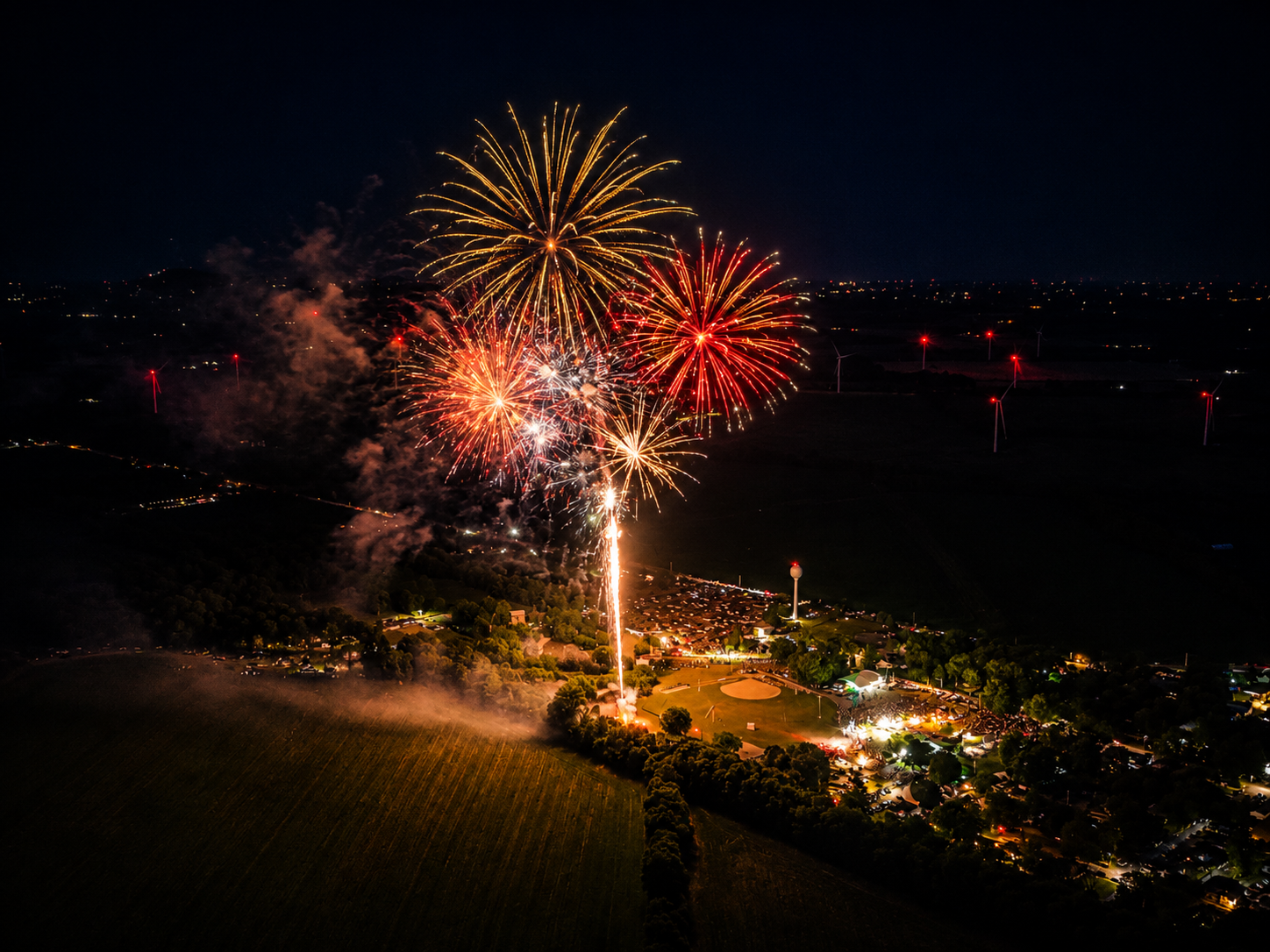 Aerial view of vibrant red and gold fireworks bursting over a rural town