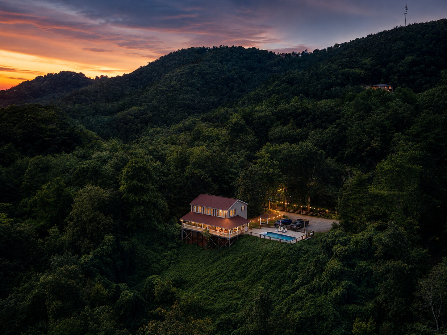 Aerial view of mountainside home with pool at sunset surrounded by forest