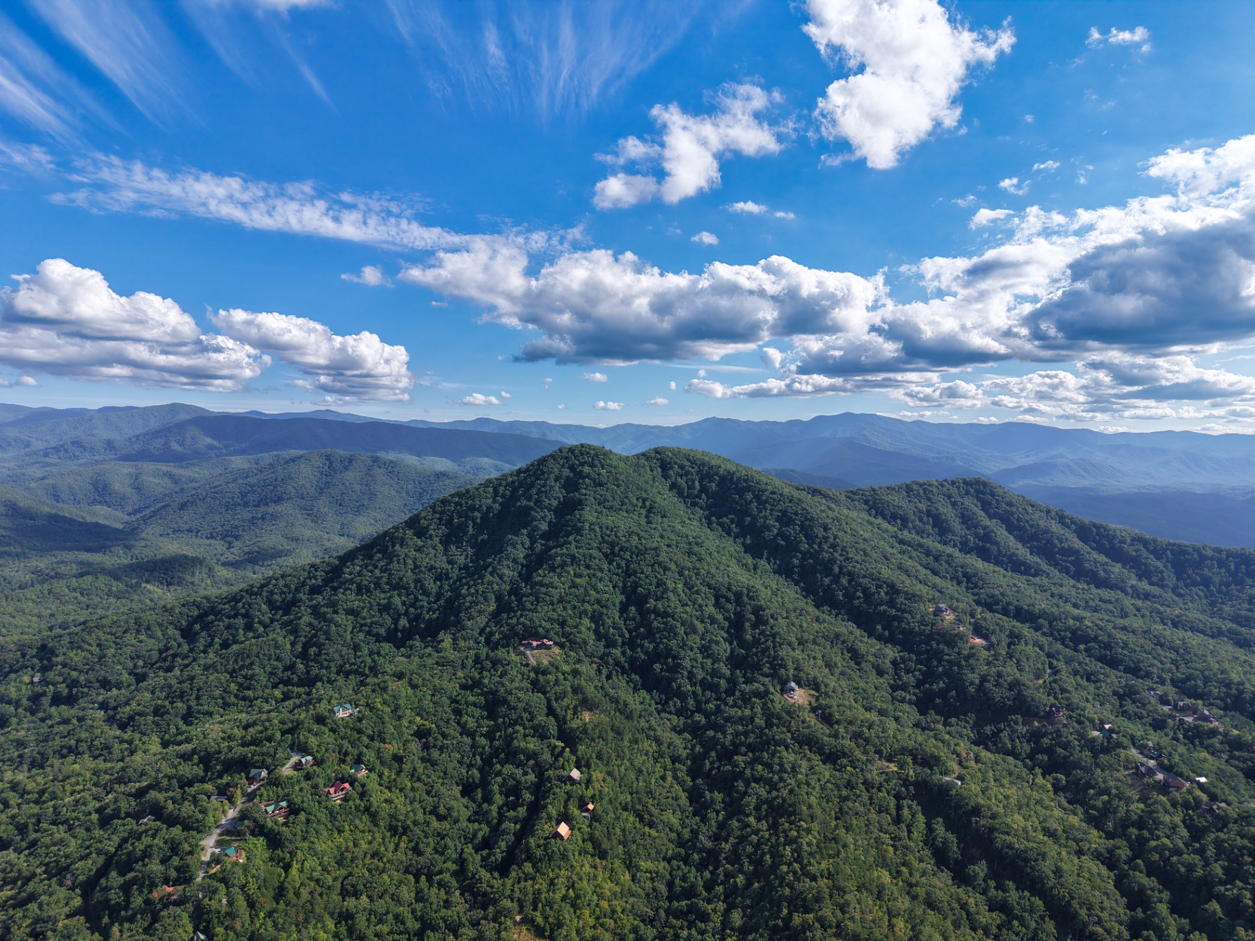 Aerial view of lush green Smoky Mountain peak with cabins and blue ridge horizon