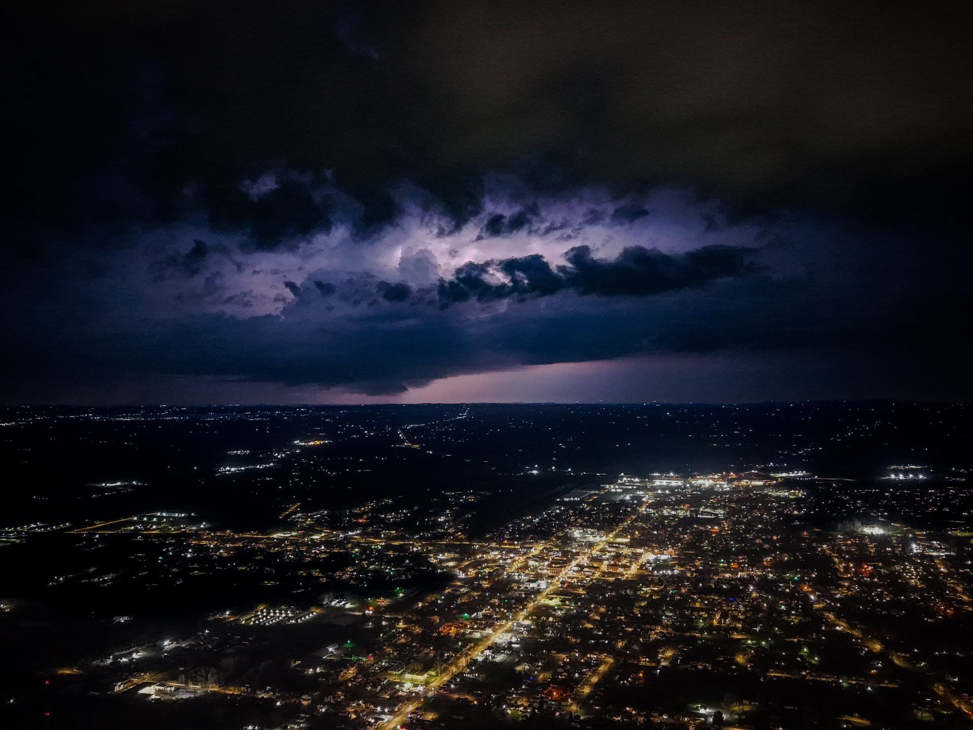 Aerial night view of city lights under a dramatic lightning storm