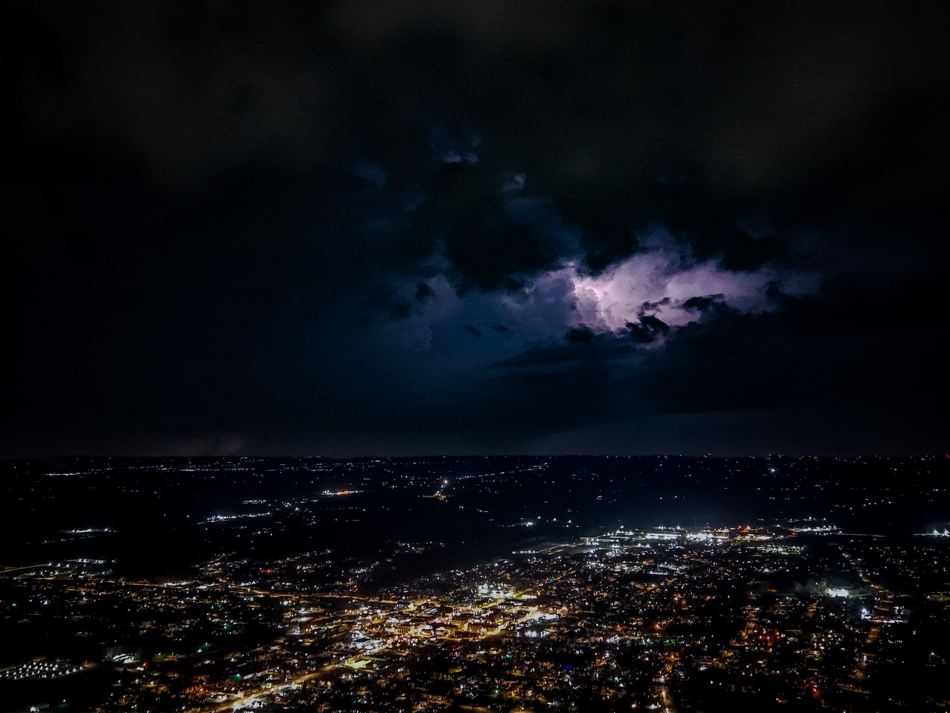 Aerial view of city at night with lightning illuminating storm clouds